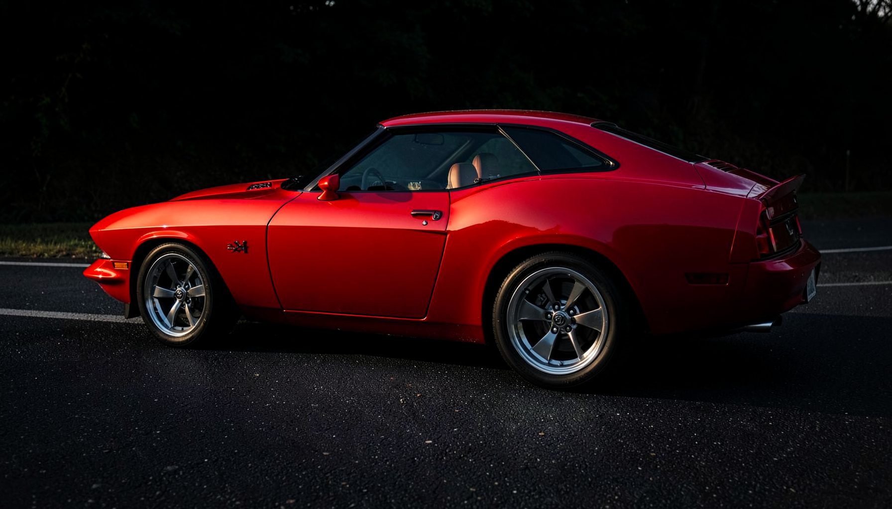 Bold red Dodge muscle car coupe on a dark asphalt road, dramatic side lighting emphasizing the sculpted body lines, powerful and aggressive mood