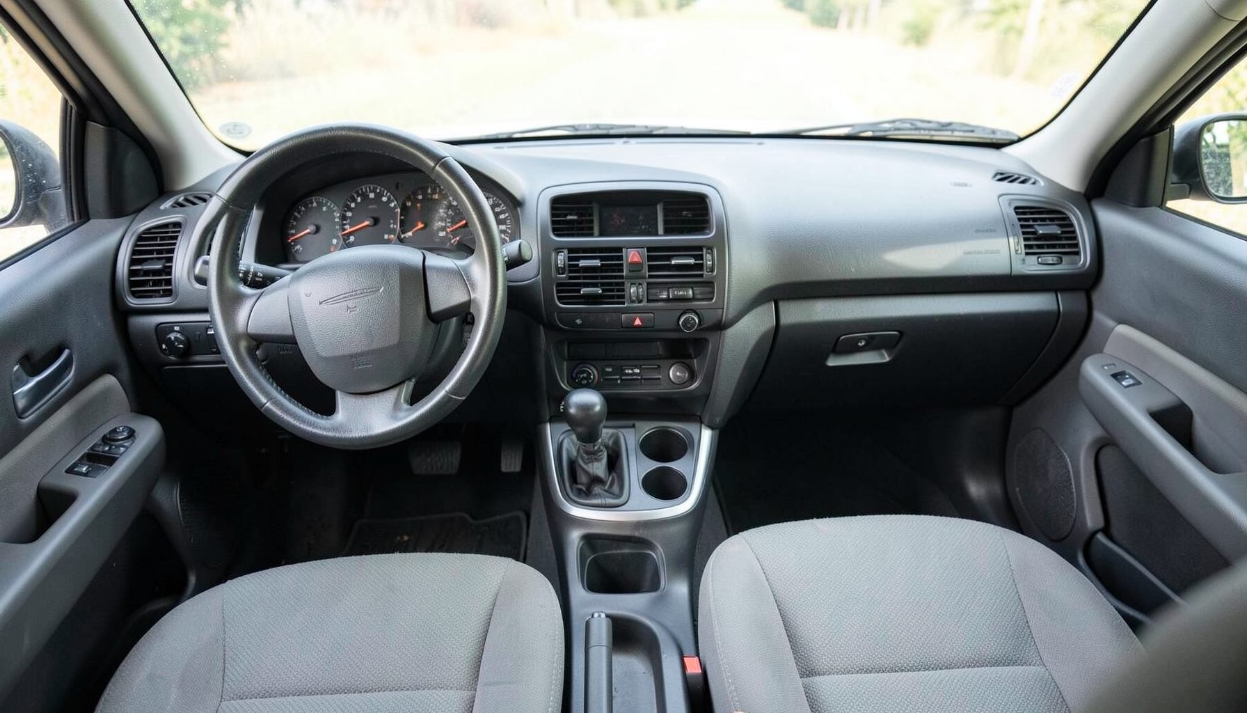 Interior view of a clean, well-maintained used car dashboard and cloth seats in neutral gray tones, with soft natural light coming through the windshield