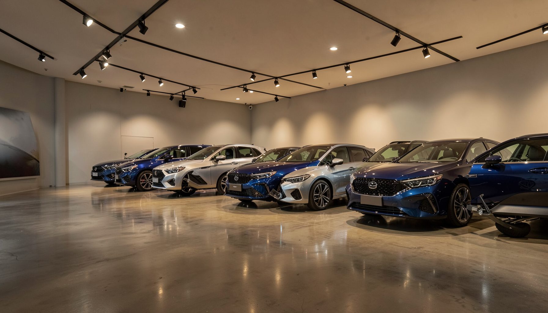 Modern automotive showroom interior with warm overhead lighting, polished concrete floors, and a row of vehicles in deep blue and silver tones under soft spotlights
